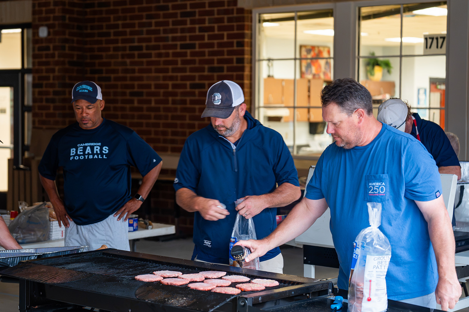 Volunteers grilling burger patties on a flat top griddle at the Cambridge Bears team dinner