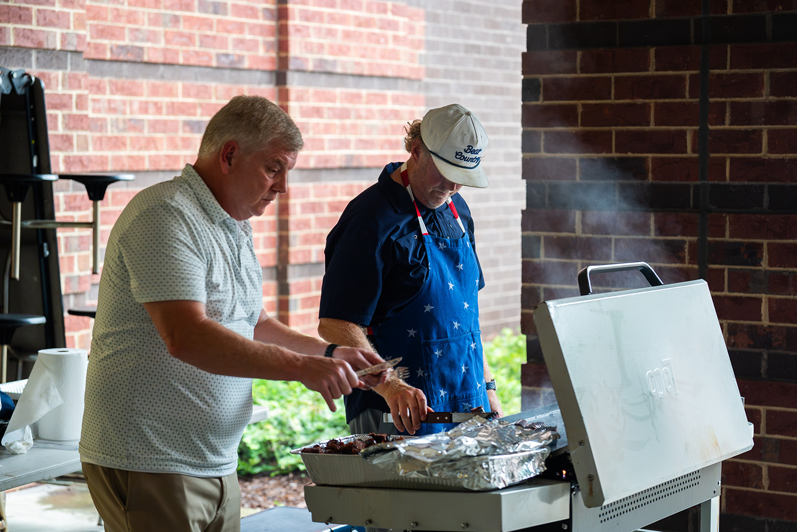 Two volunteers working the grill with trays of barbecue at the team dinner