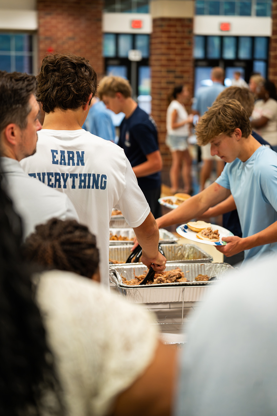 Players serving pulled pork sandwiches in the buffet line, one wearing an Earn Everything shirt
