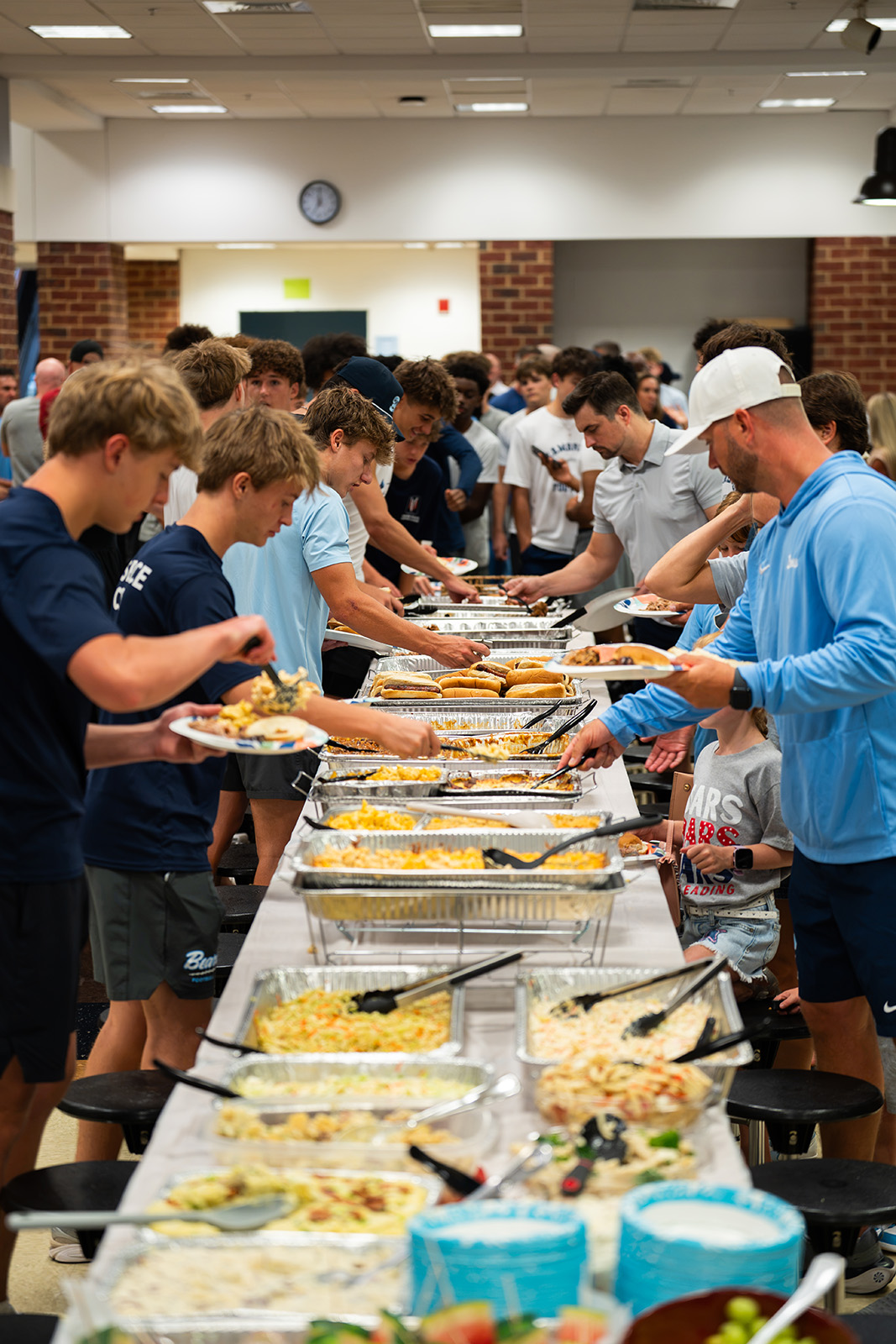 Cambridge Bears players and families serving plates down a long buffet line at the team dinner