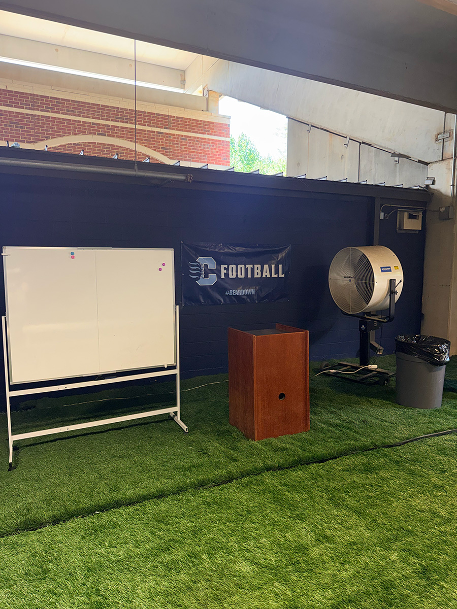 Reorganized Bear Cave meeting area with whiteboard, podium, and cooling fan on the turf