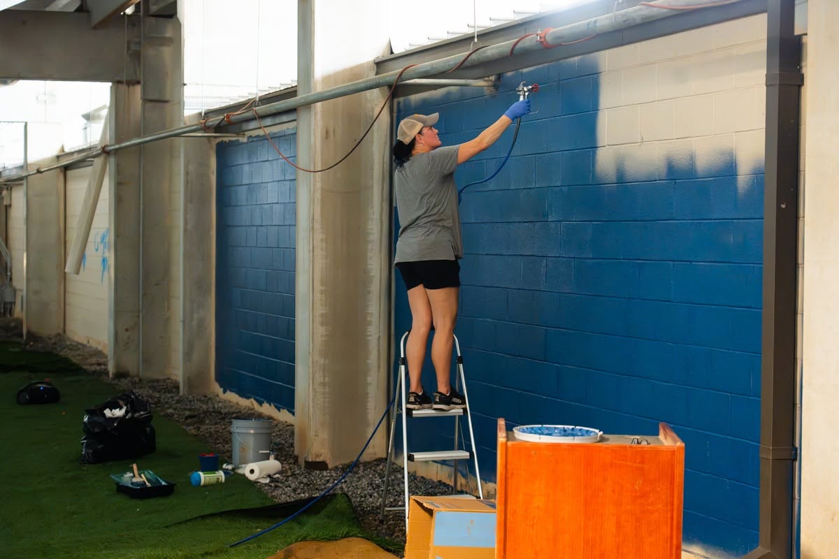 Volunteer spray-painting the Bear Cave walls Bear blue during the Bear Gridiron Club work day