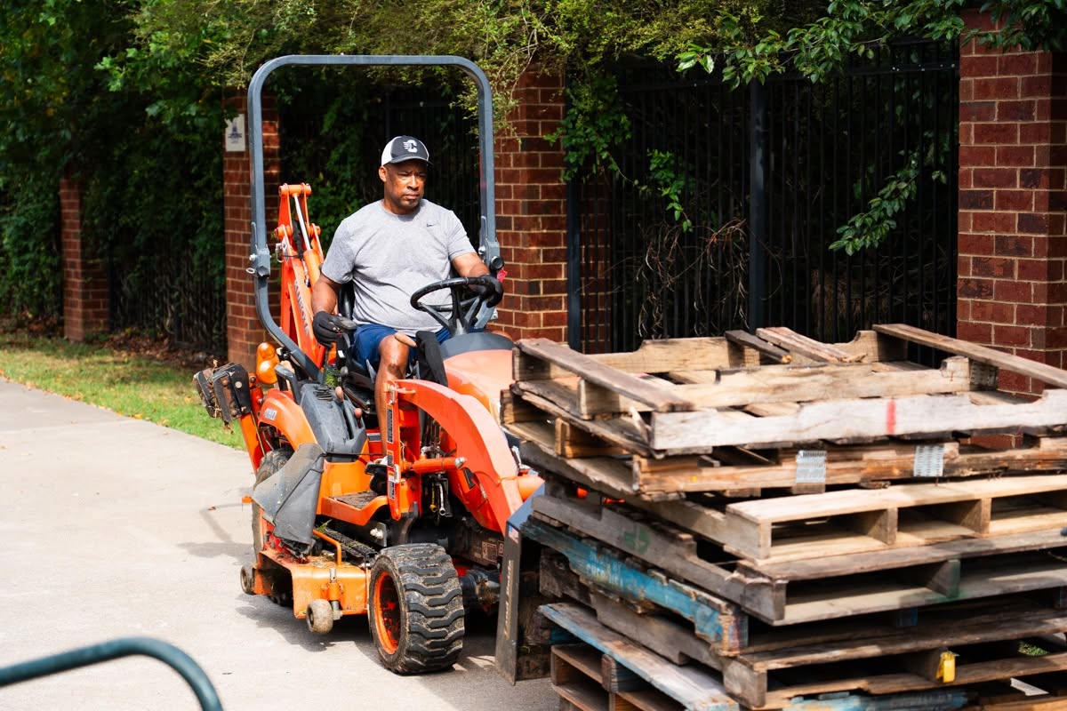 Bear Gridiron Club member moving a stack of wooden pallets with a tractor during the stadium clean-up